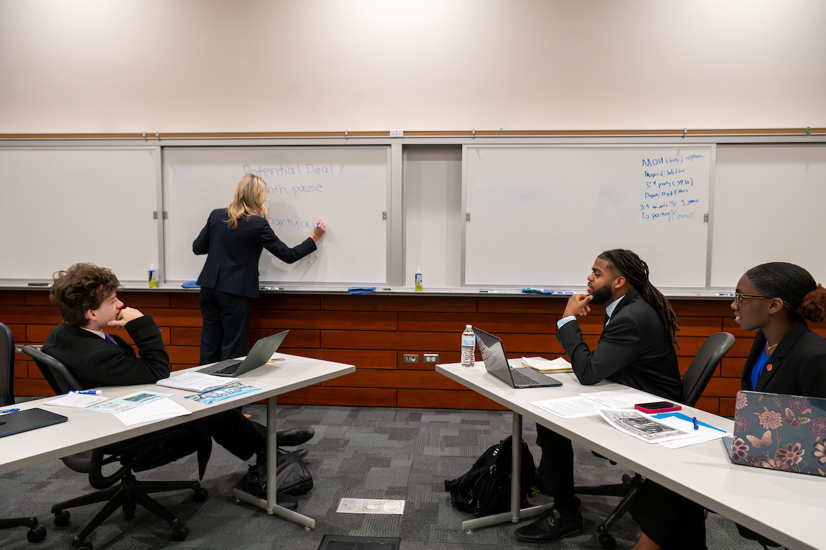 people sitting at a table having conversation and one person writing on a whiteboard
